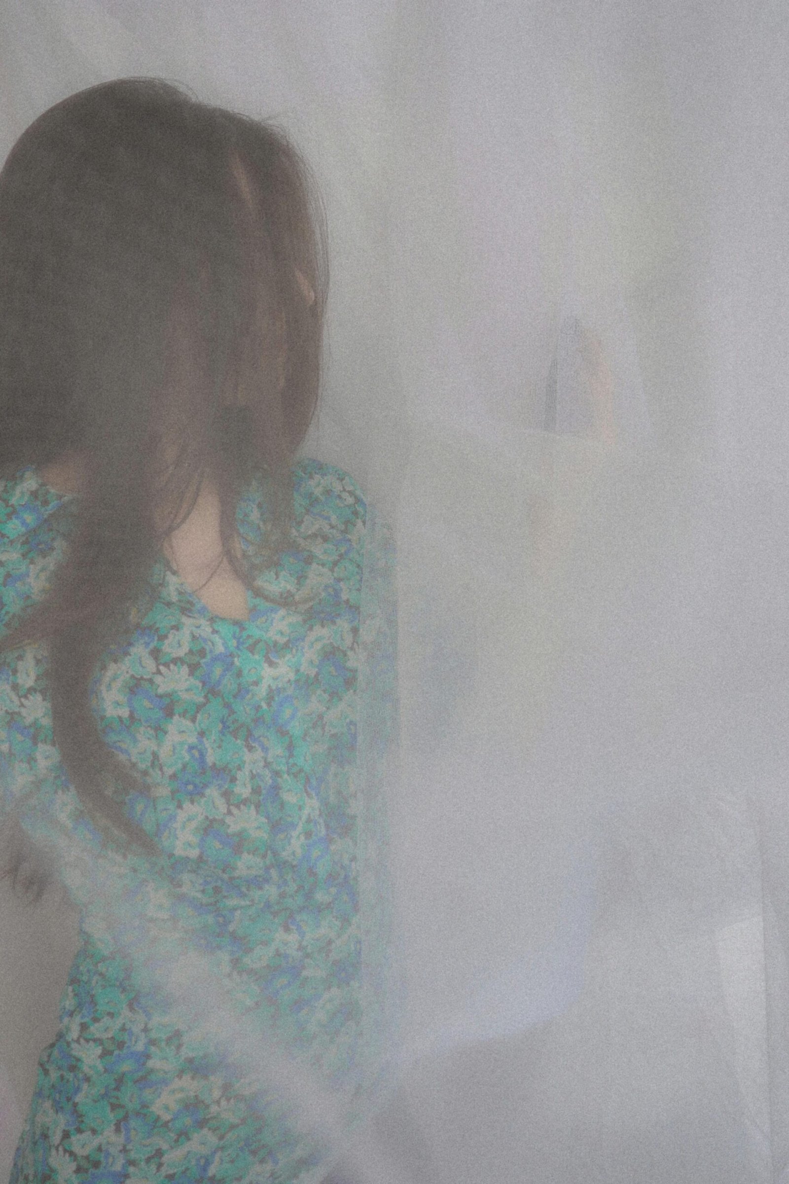 Artistic portrait of a woman in a floral dress behind a sheer curtain, creating a dreamy aesthetic.