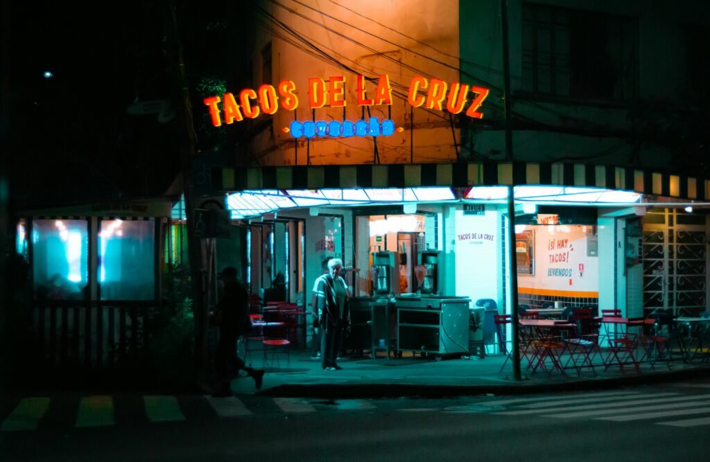 A vibrant taco stand 'Tacos de la Cruz' glowing under neon lights in Mexico City.
